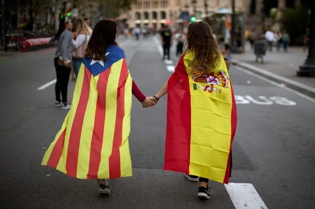Dos chicas con banderas de Catalu&ntilde;a y Espa&ntilde;a cogidas de la mano. 

"El di&aacute;logo es la &uacute;nica opci&oacute;n para frenar la escalda del conflicto catal&aacute;n"
(Emilio Morenatti/AP)