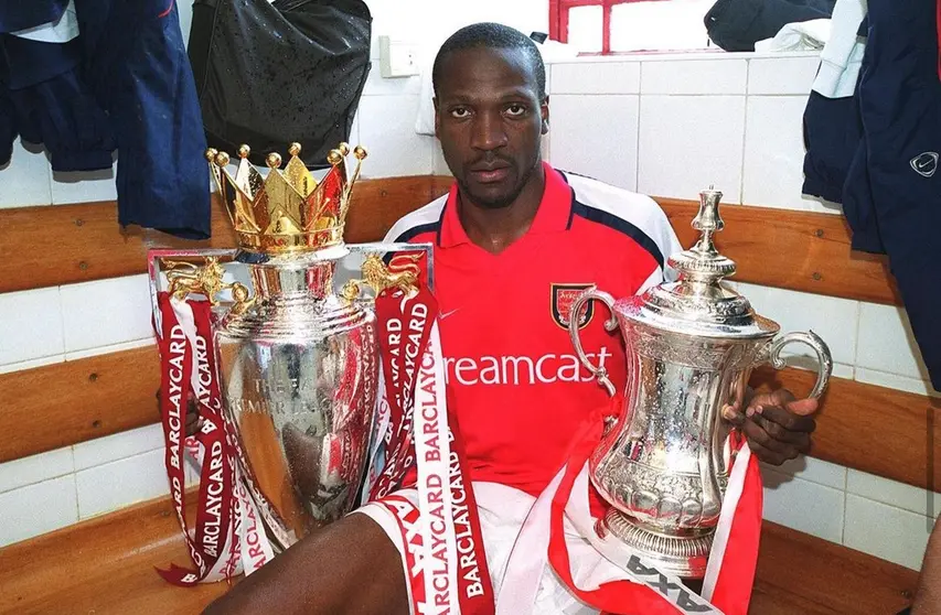 Lauren sujetando las copas de la Premier League temporada 2003-2004 y la Emirates FA Cup de 2005.