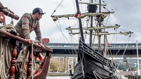 Una persona observa la r&eacute;plica de la Nao Victoria embarcando en el muelle. Extraida de Araba Press.