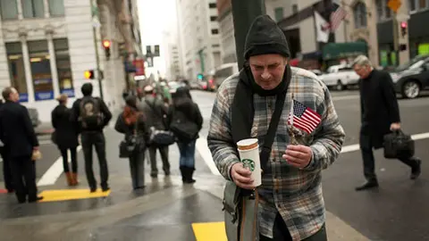 Pobre en EEUU con un vaso de Starbucks y una bandera de dicho pa&iacute;s en las manos