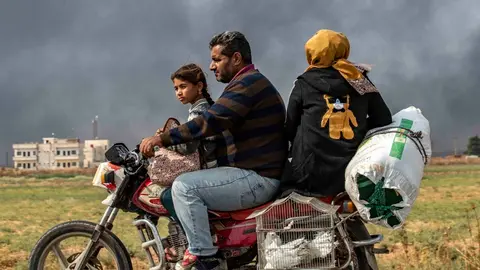 Members of a Syrian family use a motorcycle to flee the countryside of the northeastern Syrian town of Ras al-Ain on the Turkish border, toward the west to the town of Tal Tamr on October 19, 2019. The smoke behind them is from burning tyres used to impede visibility from warplanes. - Turkey's President Recep Tayyip Erdogan fired off a fresh warning today to "crush" Kurdish forces as both sides traded accusations of violating a US-brokered truce deal in northeastern Syria. (Photo by Delil SOULEIMAN / AFP)