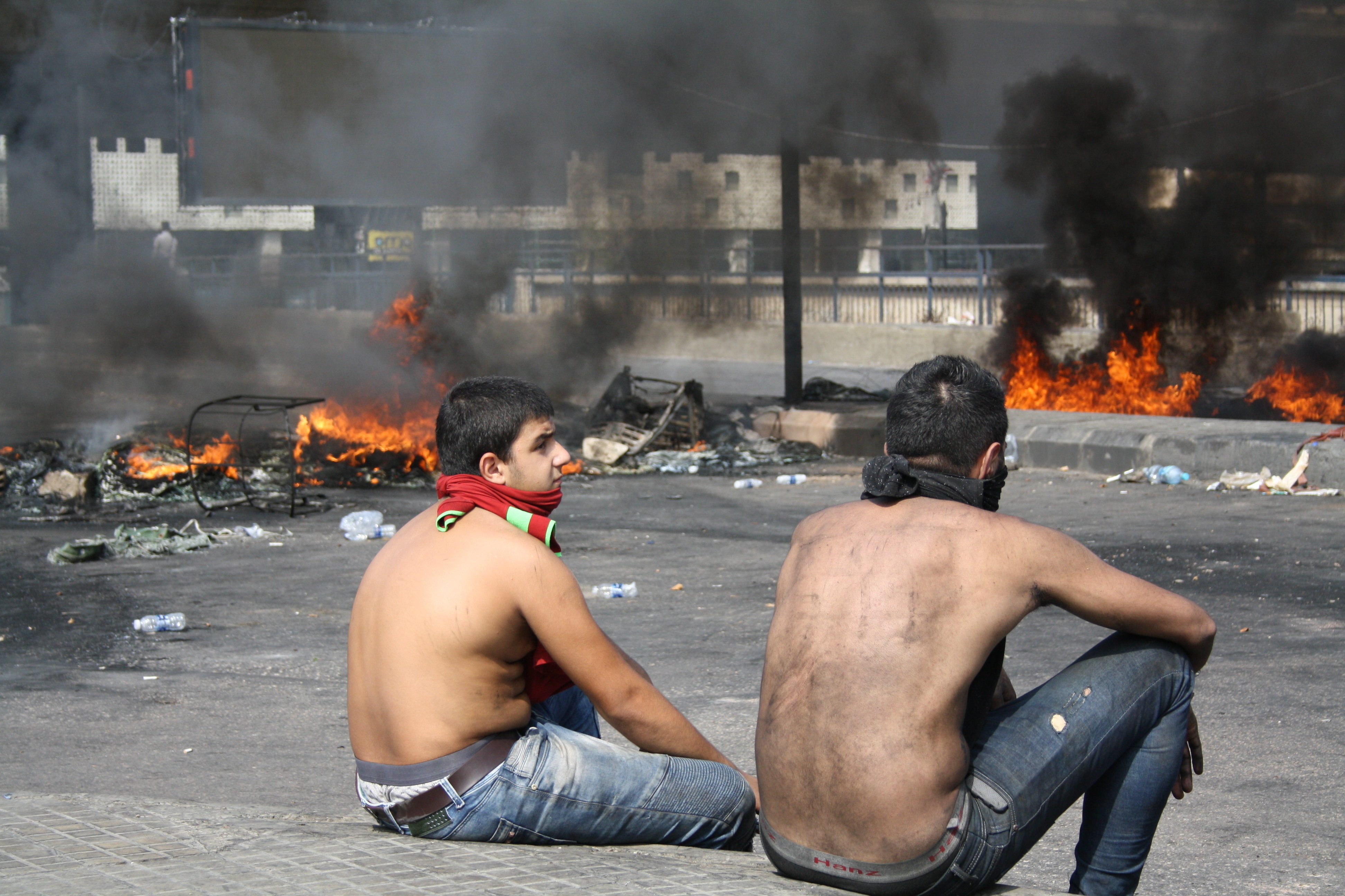 Jóvenes libaneses sentados mientras se produce un fuego en la parte del fondo de la fotografía